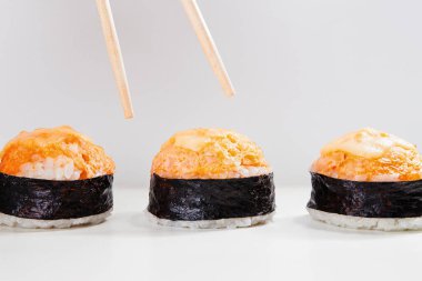 Baharatlı bir fırında sushi nigiri ya da beyaz arka planda somon balığı Gunkan üçlüsünden bir parça seçmek için yerleştirilmiş yemek çubukları havası
