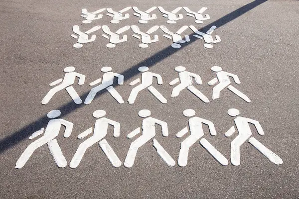 White painted symbols of people walking on a gray asphalt road indicating a pedestrian lane. Creative road sign