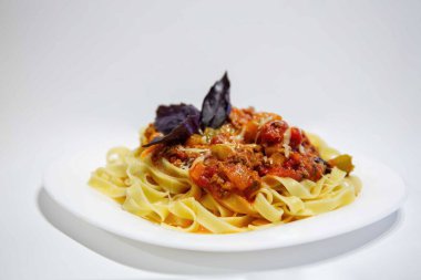 Bir tabak bolonez beyaz arka planda fesleğenle süslenir.