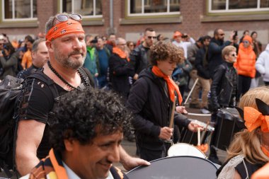 Davullu müzisyenler bir geçit törenine katılıyor. Turuncu giyerek, enerjik bir Krallar Günü kutlamasında çalıyorlar Hollanda, Amsterdam, 27.04.2023