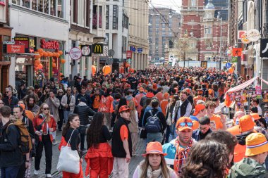 Birçok insan büyük bir festival sırasında bir caddeyi doldurur. Parlak turuncu giyerek şehirde Kral Günü 'nü kutluyorlar Hollanda, Amsterdam, 27.04.2023