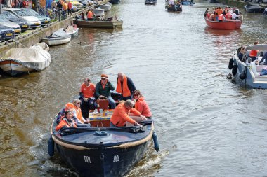 Turuncu giysili bir grup teknede kutlama yapıyor. Amsterdam 'da güneşli bir günün tadını çıkarıyorlar - Hollanda, Amsterdam, 27.04.2023
