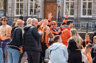 Canlı turuncu renkteki parti katılımcıları bir teknede kutlama yapıyorlar, gülümseyip el sallıyorlar, kanaldaki Kral Bayramı şenlikleri Hollanda, Amsterdam, 27.04.2023