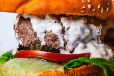 Biftek köfteli sulu çizburger, marul, domates, turşu ve kremalı sos, hepsi susamlı çöreğin arasına sıkıştırılmış.