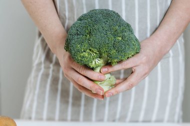 İki elinde taze brokoli floreti olan, yemek yapmaya hazır, çizgili önlüklü birinin yakın plan fotoğrafı..