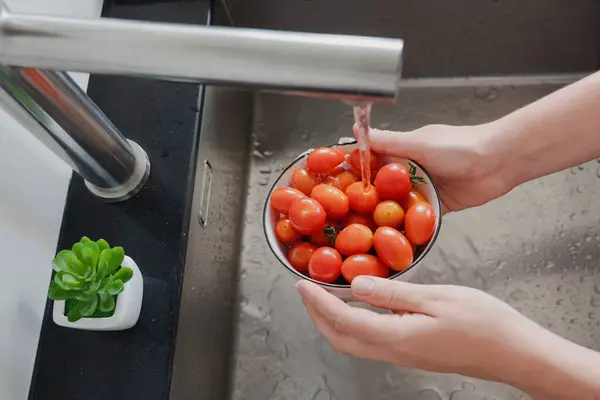 stock image Hands washing a bowl of fresh cherry tomatoes under running tap water in a kitchen sink