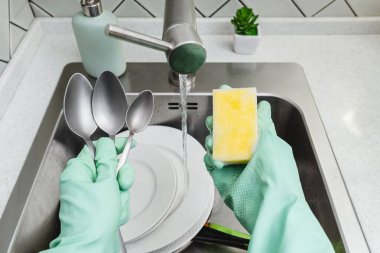Ellerinde sünger ve kap kacak tutan yeşil eldivenler, mutfakta paslanmaz çelik bir lavaboda bulaşık yıkıyorlar. Ev temizliği ve hijyen