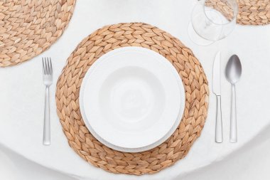 Beyaz tabaklar, dokuma kaplar ve gümüş çatal bıçak takımlarıyla yemek masası manzarası.