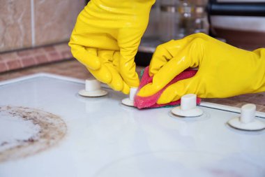 Sarı eldivenli eller soba topuzlarını süngerle fırçalamak, ev temizliği.