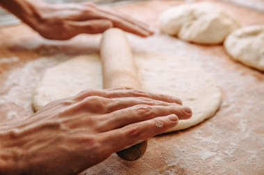 Elleri hamuru ahşap bir oklavayla un kaplı bir yüzeyde yuvarlıyor, ev yapımı ekmek ya da pizza yapıyor.