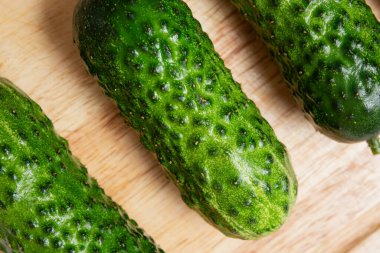 Tahta bir kesme tahtasına yerleştirilmiş taze yeşil salatalıkların yakın çekimi. Salatalık kabuğu dokusu