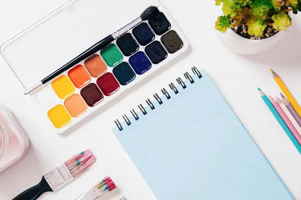 stock image Blank notebook lies next to watercolor paints, brushes, and colored pencils, top view isometric mockup