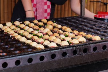 Şefin siyah eldivenleri takoyaki pişiriyor, Japon aperatifleri, içinde ahtapot parçacıkları olan hamur şekilli sıcak bir tavada.