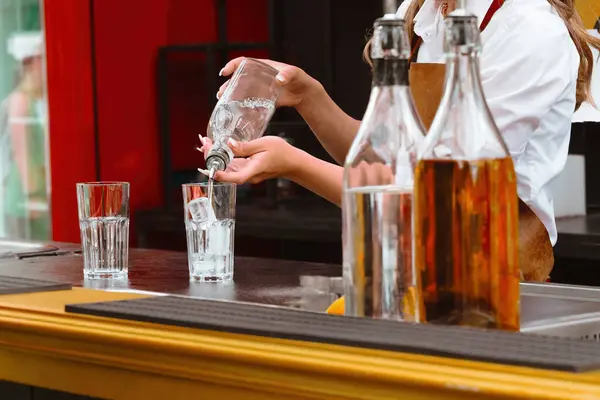 stock image A bartender in apron preparing a cocktail in glass with ice at a bar