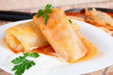 Sığır eti ve sebzeyle dolu lahana ruloları maydanozla süslenmiş ve domates sosunda ekşi kremayla servis edilmiş.