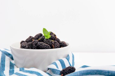 A white bowl filled with fresh blackberries topped with a mint leaf, elegant summer berry snack clipart