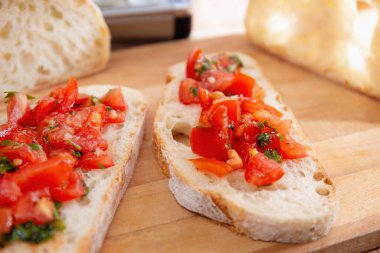 Domatesli bruschetta 'ya yakın plan ekmek dilimleri, taze doğranmış domatesler ve ahşap bir tahtanın üzerinde otlar.