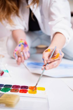 Ressamın elleri boyayla kaplıyken, suluboya bir fırça kullanarak, yaratıcılığı ve sanatsal ifadeyi göstererek,.