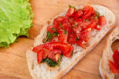 Dilimlenmiş ekmeğin üzerinde taze domates bruschetta, doğranmış domates, şifalı otlar ve ahşap bir tahtanın üzerinde marul..