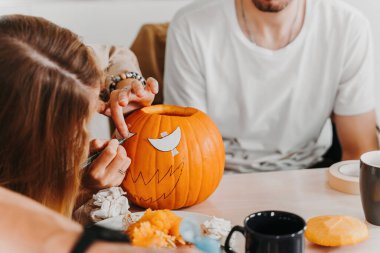 Cadılar Bayramı 'na hazırlanmak için balkabağına bir yüz dizaynının izini sürmek için şablon kullanan iki kişinin yakın plan fotoğrafı.