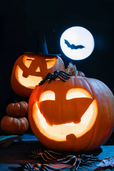 stock image Two glowing Jack-O'-Lanterns, pumpkin scary faces, full moon and bat in the background, creating a spooky Halloween scene