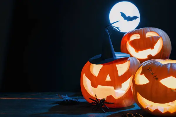 stock image Three carved, glowing pumpkins, dark Halloween background with full moon and bat silhouette