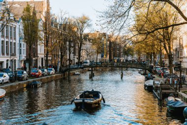 Amsterdam 'da, Hollanda, Amsterdam, 12.11.2022 tarihli tarihi binalarla çevrili sakin bir kanalda küçük bir tekne geziniyor.