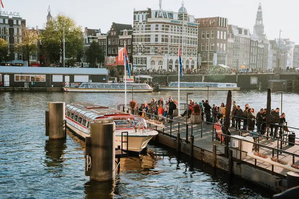 stock image Tourists on a dock in Amsterdam, waiting to board a canal boat, historic buildings and boats in background - Netherlands, Amsterdam,12.11.2022