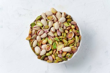 Yeşil ve mor şam fıstıklarıyla dolu, kabuklu ve kabuksuz beyaz bir kâse.