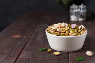 White bowl of pistachios on a dark wooden table with scattered nuts, bar table, beer snack clipart