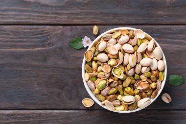 Shelled and unshelled Pistachios filled white bowl placed on a dark wooden rustic table clipart