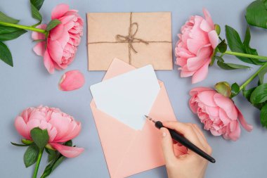 Zarfın içindeki boş karta bir kalem, pembe şakayık çiçeği süslemesi ve mektup zarfına el yazısı.