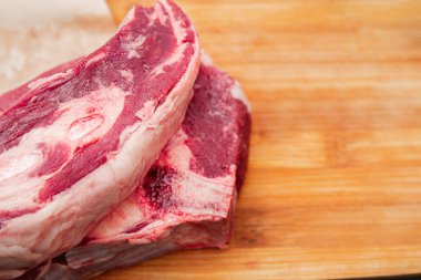 Ahşap bir kesme tahtasının üzerinde duran, ızgaraya ya da pişirmeye hazır, büyük, çiğ bir biftek.