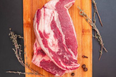 Tahta kesim tahtasında çiğ biftek, kekik filizi ve biber, pişirmeye ve baharata hazır.