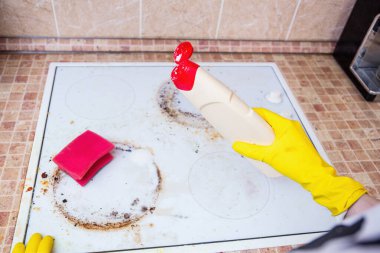 Sarı eldivenler kirli bir sobanın üzerinde temizlik deterjanı tutuyor. Süngerle ovalanmaya hazır.