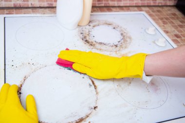 Sarı eldivenli, deterjanlı, süngerli, kirli cam seramik tencereli, mutfak hijyenli biri.