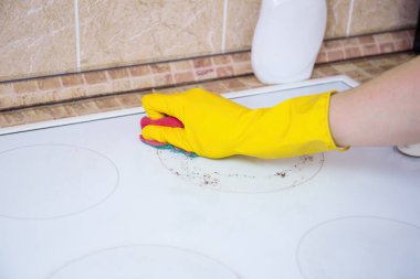 Sarı eldivenli, deterjanlı, süngerli, kirli cam seramik tencereli, mutfak hijyenli biri.