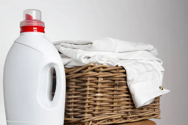 stock image Laundry basket filled with stack of folded white clothes, detergent bottle mockup, laundry day and clothing care