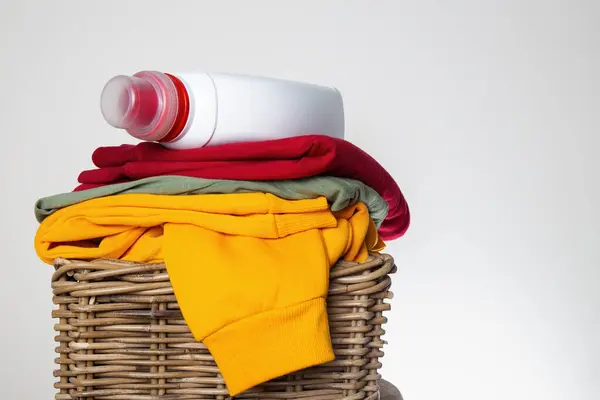 stock image Stack of colorful folded clothes in a wicker basket with a detergent bottle on top, ready for laundry day