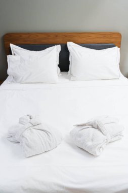 İki katlanmış bornoz, temiz beyaz bir yatakta, yumuşak çarşaflı, spa benzeri bir konfor, rahatlama ve huzurlu bir uyku gecesi sunuyor.