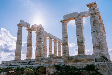 Ancient columns of the Temple of Poseidon rise high under bright sky, sunburst, at Cape Sounion, symbol of Greek history clipart