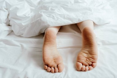 Huzurlu bir sabah rahat bir yatak odasında beyaz çarşafların altından bir çift çıplak ayak, uyku kalitesi.