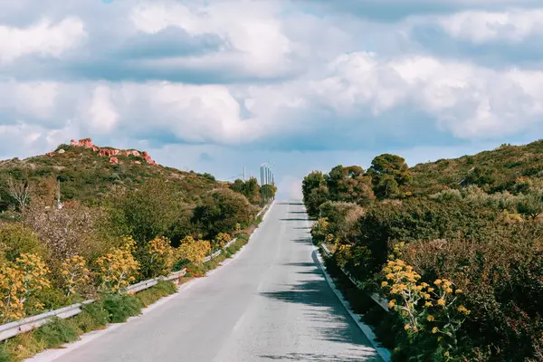 stock image Scenic empty road with road markings leading through hills with yellow flowers and into horizon with dramatic cloud sky