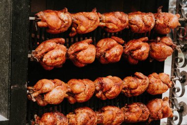 Rows of whole roasted chickens turning on skewers over a rotisserie flame, golden-brown chickens on rotisserie grill outdoors clipart