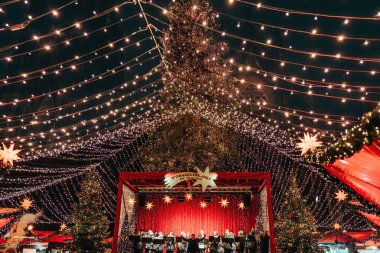 Almanya, Köln, 12.10.2022 - Büyük dekore edilmiş ağaç ve kırmızı market tezgahlarının yer aldığı festival ışıkları altında Noel pazar konseri sahnesi