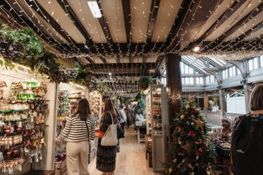 Birleşik Krallık, Londra, 10.16.2024 - müşteriler mağazada çeşitli Noel süslerine bakıyorlar, başlarının üzerinde çelenkler ve tatil ışıkları asılı