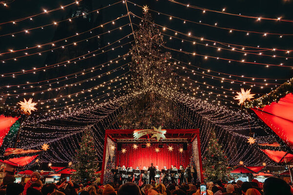 Германия, Кёльн, 12.10.2022 - Хор поет на рождественской сцене в Кёльне, большая толпа, с праздничными огнями