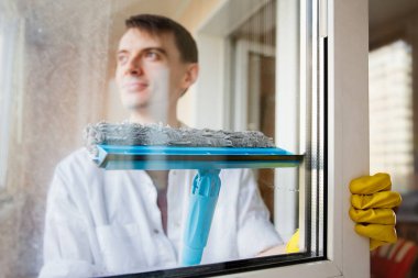 Sarı eldivenli bir adam cam silici ile pencereyi siler, bahar pencerelerini temizler.