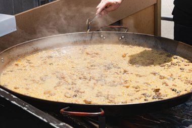 Pilav, tavuk ve mantardan yapılmış büyük tavada kaynatılmış İspanyol paellası yemek pazarında aşçı tarafından pişiriliyor.