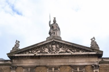 Mızrağı ve kalkanı olan taş bir heykel Londra 'da tarihi bir soyun tepesinde duruyor. Etrafı ejderha oymaları ve süslü detaylarla çevrili.